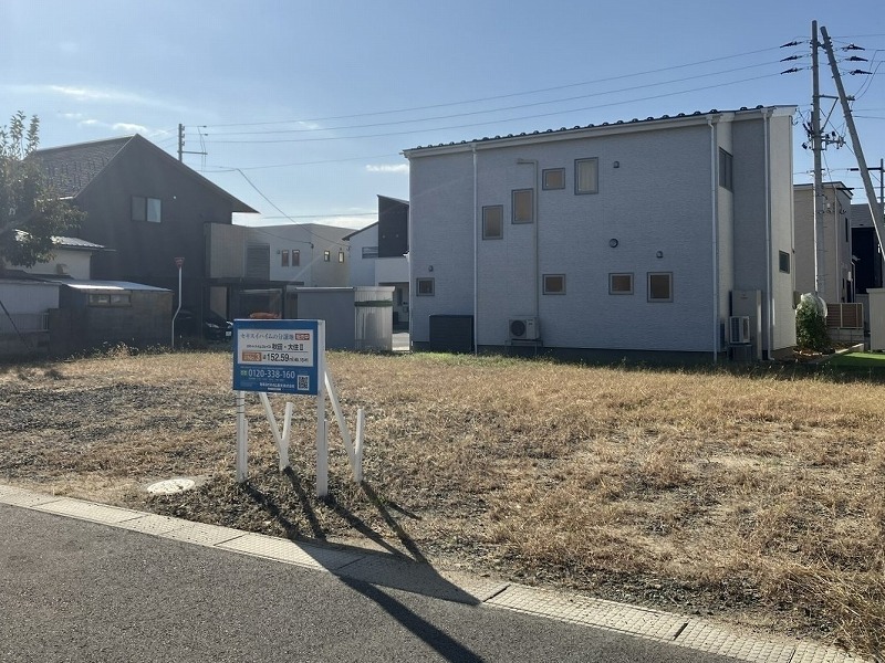新しい住宅街の一角で、電柱と道路に面した分譲地。背景には家が数軒並んでいます。