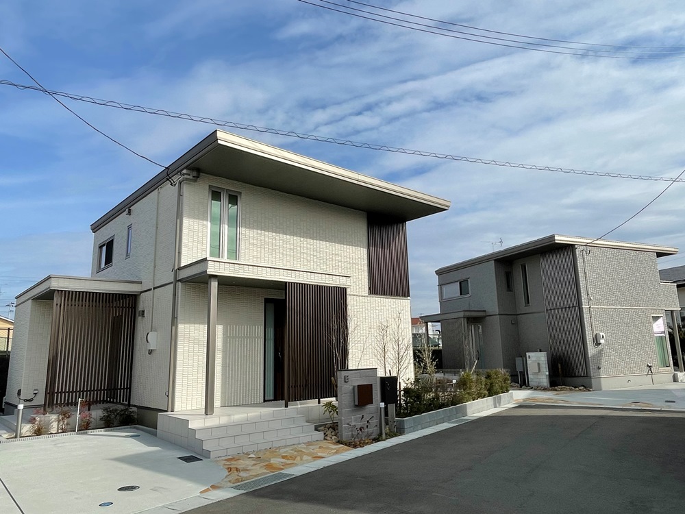 クレーと白い外壁の住宅の外観。すっきりとした直線的なデザインが特徴です。手前の家の前には植栽と玄関までの階段があり、整った外構が広がっています。