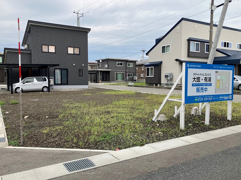 舗装された道路に面した住宅建築予定地と案内掲示板。