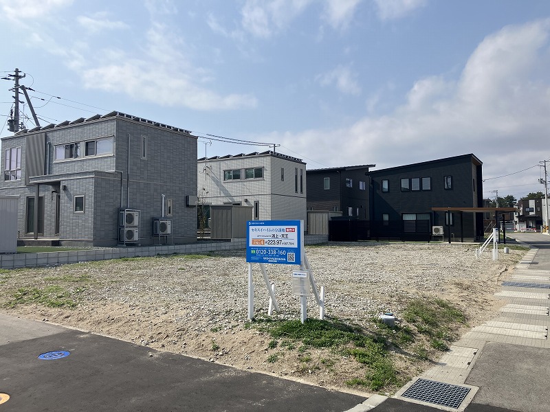 住宅地内にある分譲地。周囲には黒や白を基調としたセキスイハイムの住宅などが建ち並んでいます。道路沿いには電柱や駐車された車が見えます。