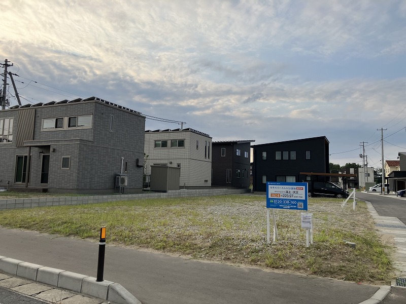 住宅地内にある分譲地。周囲には黒や白を基調としたセキスイハイムの住宅などが建ち並んでいます。道路沿いには電柱や駐車された車が見えます。