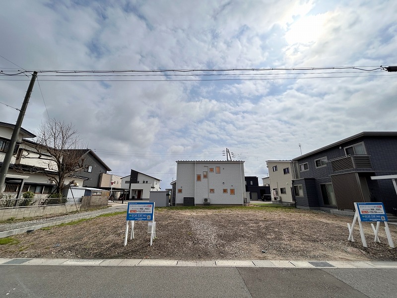 新しい住宅街の一角で、電柱と道路に面した分譲地。背景には家が数軒並んでいます。