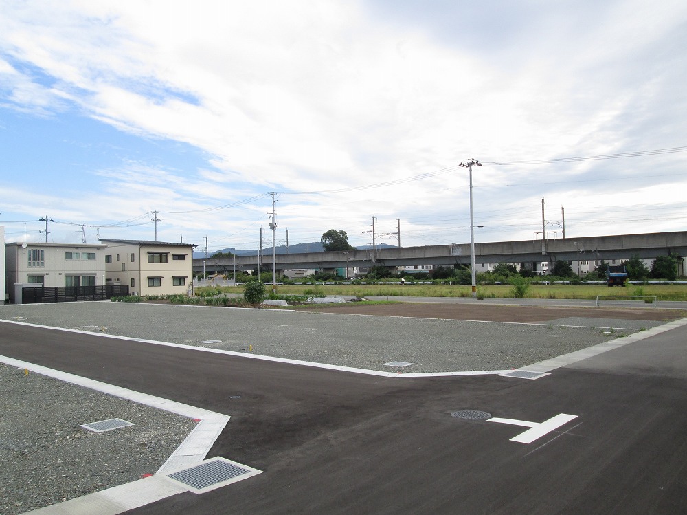 空が広がる静かな住宅地の一角に分譲地があります。奥にはいくつかの住宅が建ち、さらに遠くには高架橋が見えます。