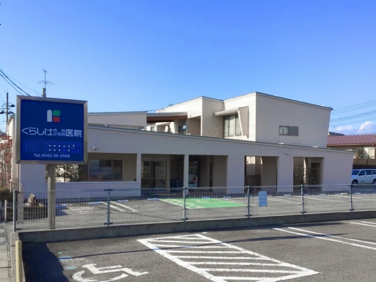 青い看板が特徴的なくらしげ内科・小児科医院の外観。駐車場とフェンスが見えます。