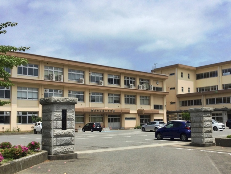 3階建ての第1中学校校舎の外観。駐車場には車が数台停められています。