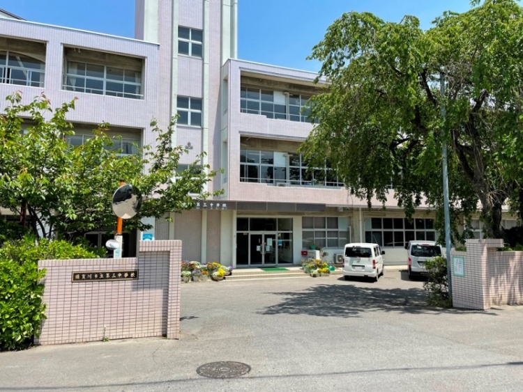 ピンク色の壁が特徴的な3階建ての須賀川市立第三中学校校舎の外観。手前に門があり、駐車場その奥に校舎が見えます。