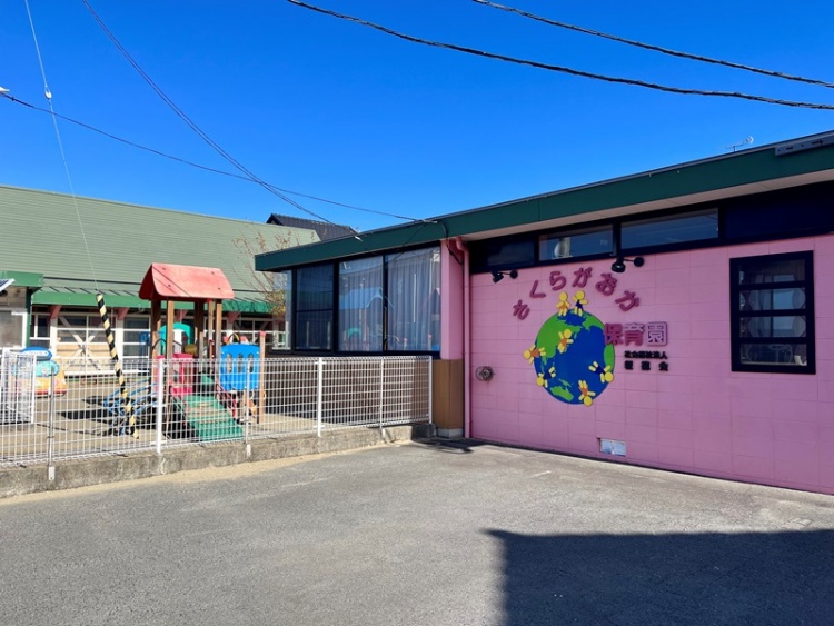ピンク色の外壁が特徴的なさくらがおか保育園の外観。フェンスの向こうには遊具が見えます。