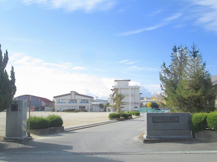 白い外壁の一関小学校校舎の外観。広い敷地に複数の建物が建っています。