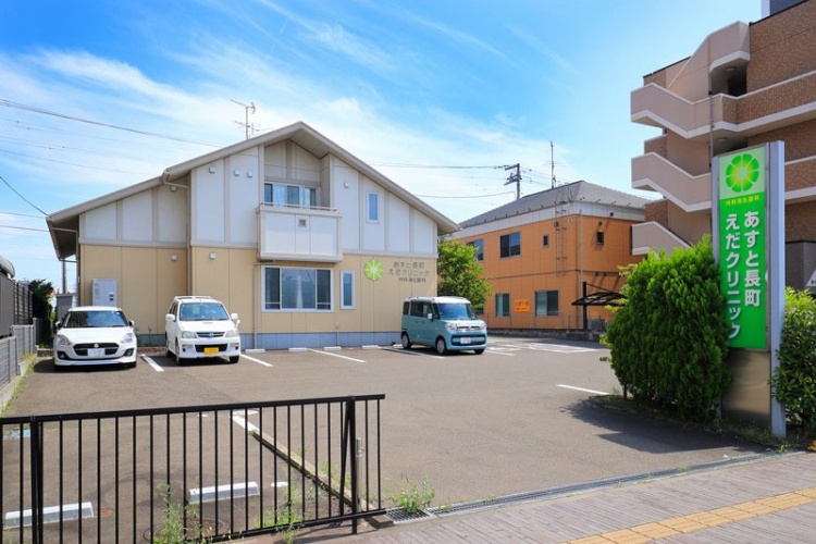 黄緑色の看板が特徴的なあすと長町えだクリニックの外観。駐車場には数台の車が停められています。