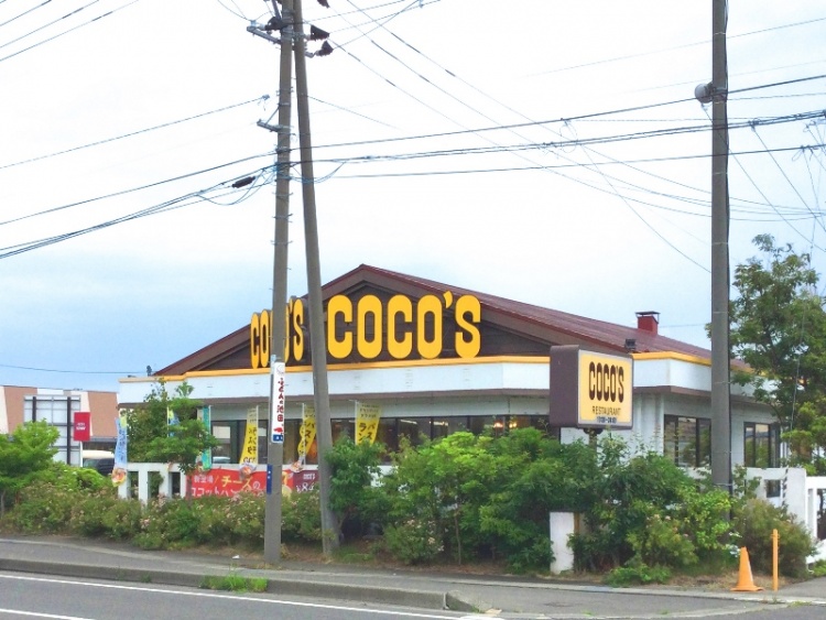 ココスの店舗外観。大きな黄色の看板に黒文字でCOCO'Sと書かれていて、前面には植栽が植えられています。
