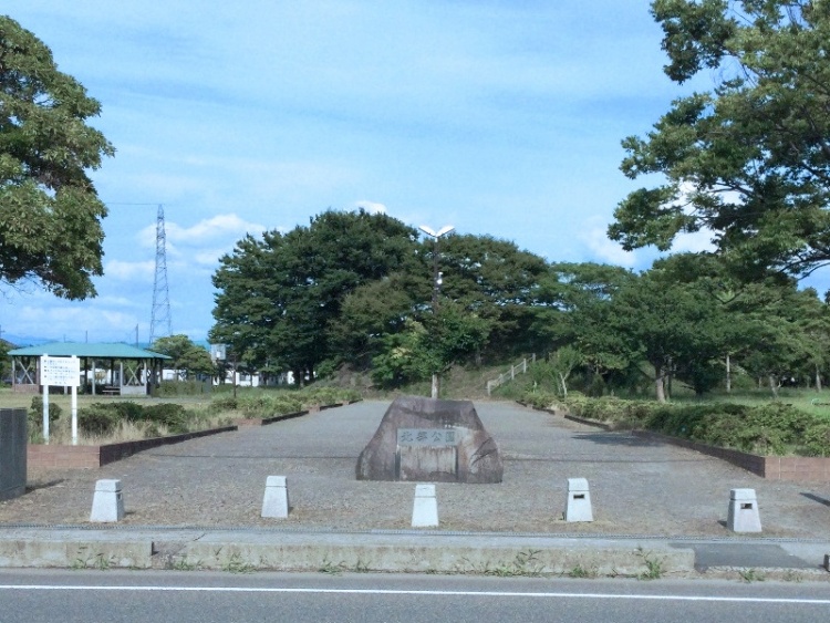 広場の中央に石碑があり、北部公園と書かれています。その奥に木々と広場のベンチが見えます。
