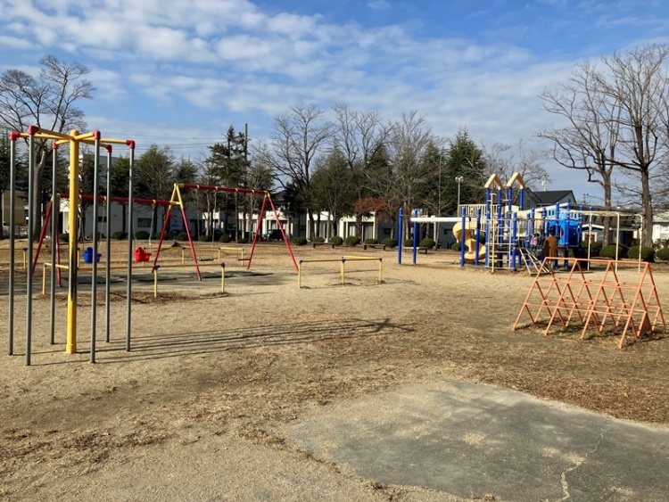 赤と黄と青が特徴的な公園。ブランコや滑り台、ジャングルジムが設置されています。背景には木々が見えます。