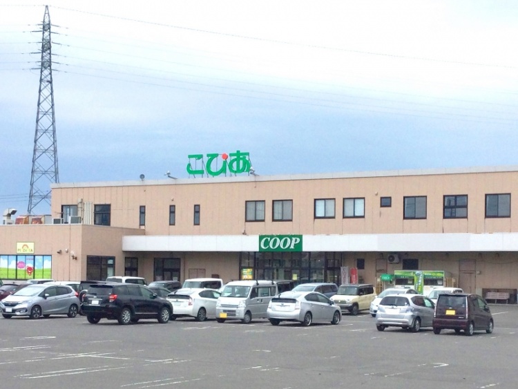 ベージュの外壁のこぴあコープ酒田の外観。手前の駐車場にはたくさんの車が停められています。