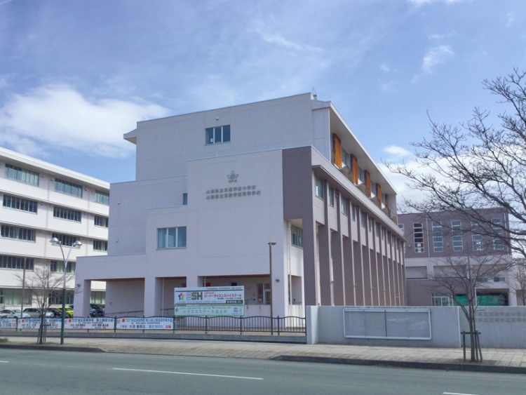 白い外壁の山形県立東桜学館の校舎の外観。校門には看板が見えます。