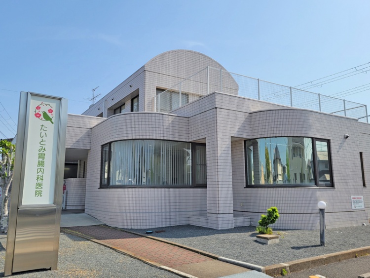 白いタイル張りの2階建てのたいとみ胃腸内科医院の外観。レンガ調の道が病院まで続いています。