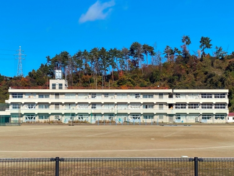 白い3階建ての一箕中学校の外観。背景に木の多い丘が見えます。