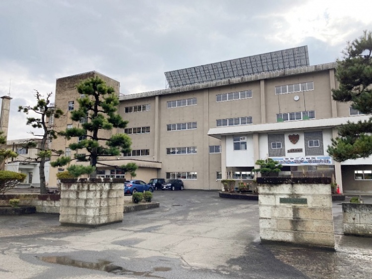3階建てで多くの窓がある大館東中学校の建物。校庭に松の木が植えられています。