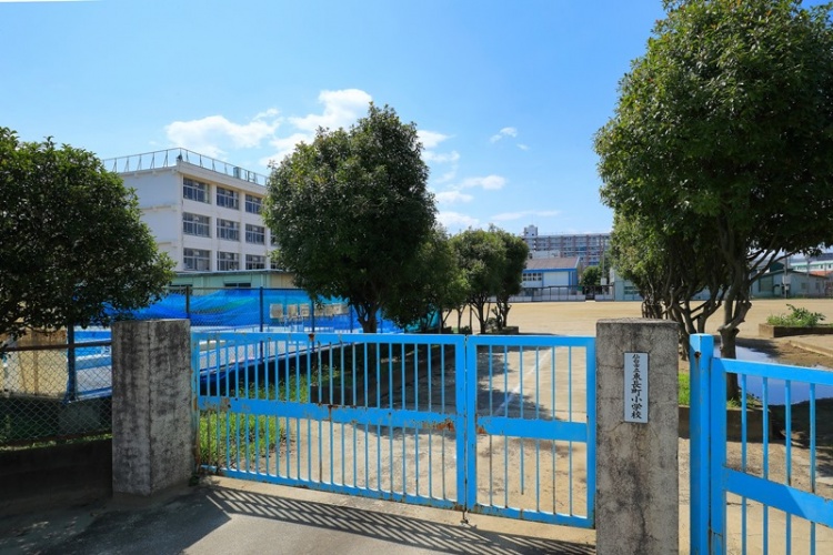 仙台市立東長町小学校校舎の外観。青い門扉と樹々が並ぶ校庭が見えます。