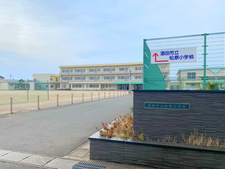 3階建ての酒田市立松原小学校校舎の外観。校庭とフェンスが見えます。