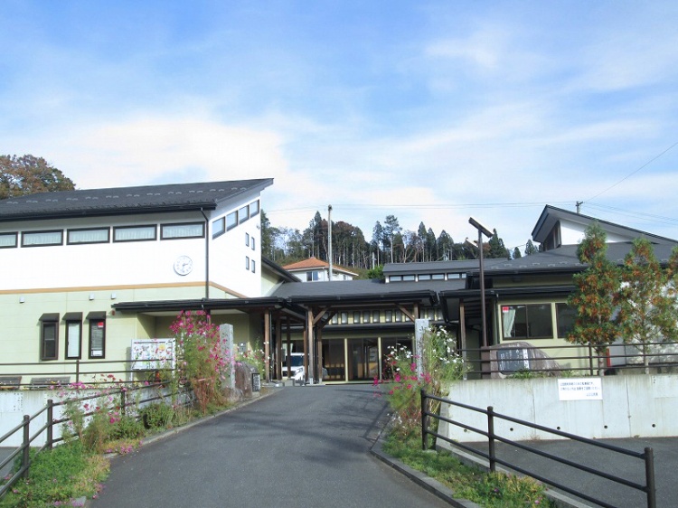 白壁の二階建ての山口公民館の外観。花が咲く通路が入り口まで伸びています。