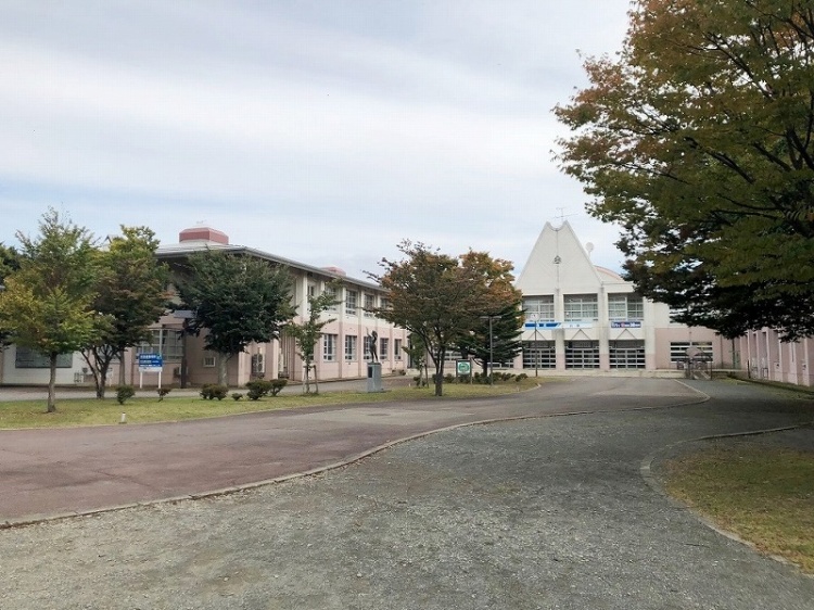 広々とした敷地に立つ天王南中学校の校舎とその周囲の風景。木々が並ぶ道が見えます。