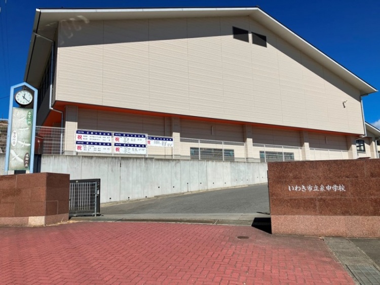 いわき市立泉中学校の校舎と入口の看板が写る写真。校舎前には赤いレンガの歩道がある。