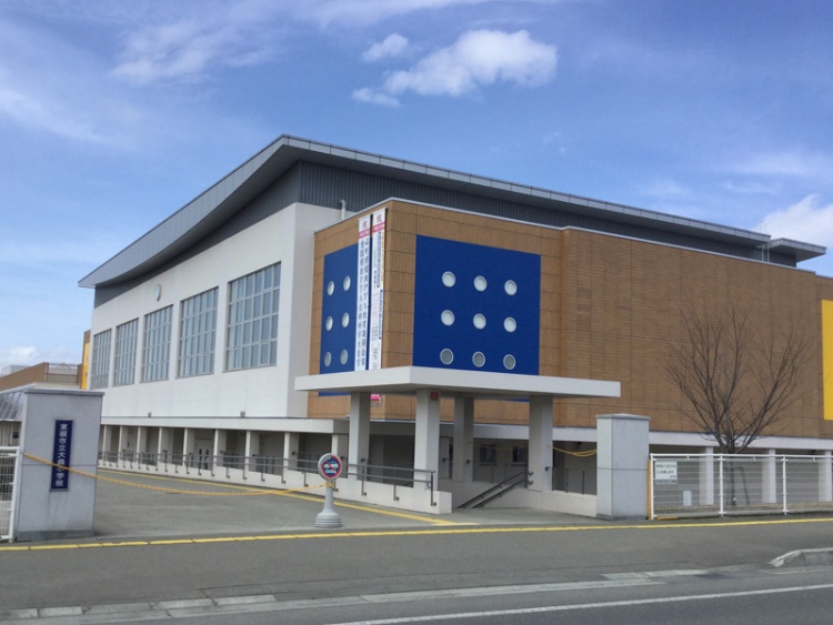 白とブラウンを基調とした東根市立大盛り小学校校舎の外観。手前には道路が見えます。
