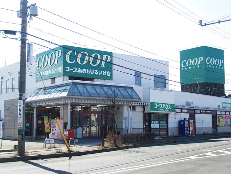 白い建物に緑色の看板が掲げられたコープあおもりるいけ店の外観です。駐車場と道路が見えます。