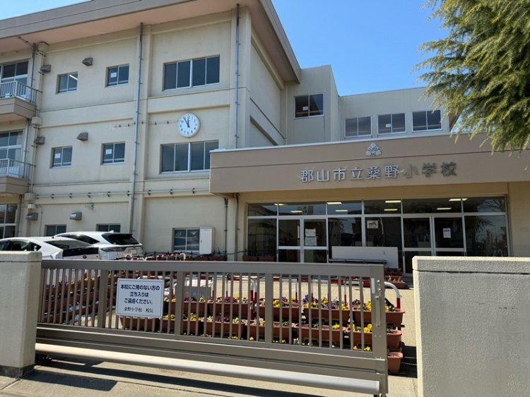 ベージュの外壁が特徴的な郡山市立桑野小学校の校舎の外観。校舎は3階建てで、庭には花壇が見えます。