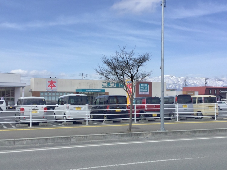 こまつ書店東根店の外観。駐車場には数台の車が停められています。背景には雪山が見えます。