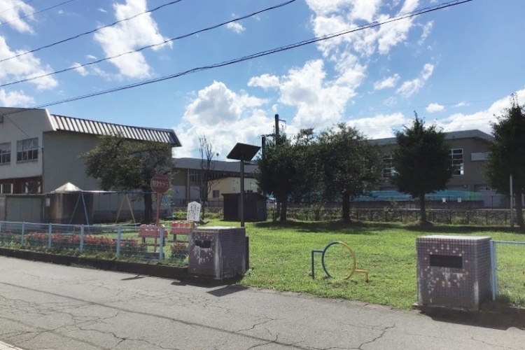 住宅街の公園で、ブランコや鉄棒などの遊具が見えていて、木々が広がっています。