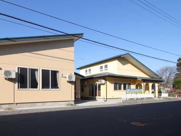 黄色い建物のキッズピーパル保育園の外観。手前には道路が見えます。