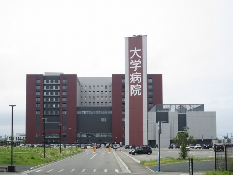 大きな「大学病院」の看板がある建物の正面玄関。駐車場が周囲に広がっている。