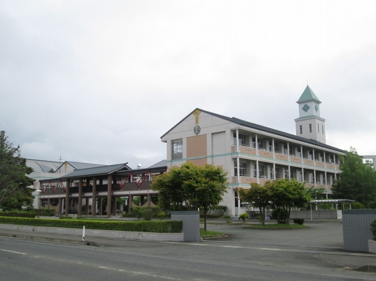 時計塔が特徴的な矢巾北中学校の校舎外観。前庭には植栽が植えられています。道路沿いに位置しています。