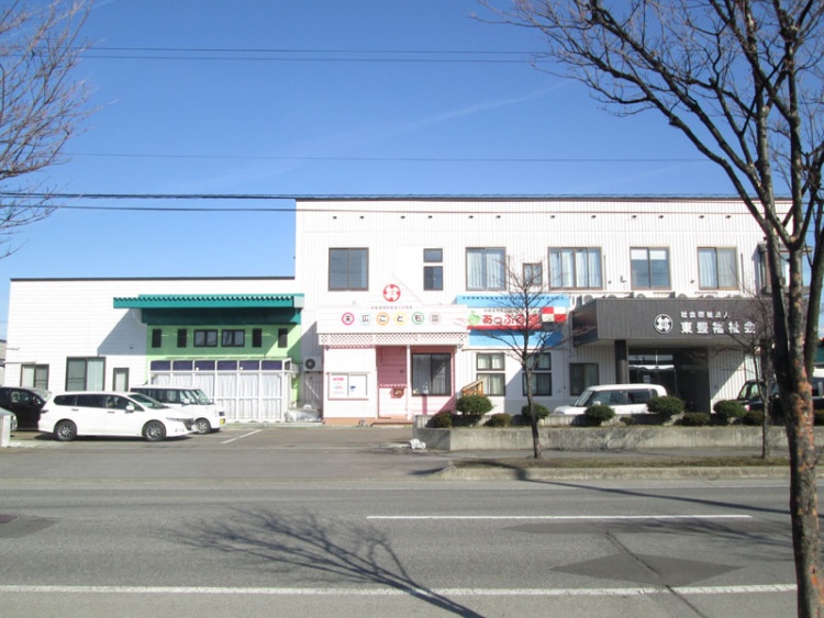 ピンク色の建物の末広子ども園の外観。前に駐車場があり、数台の車がめられています。