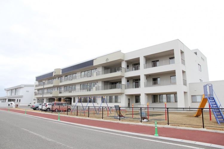 3階建ての横手北小学校の校舎と校庭の風景です。手前には道路があります。