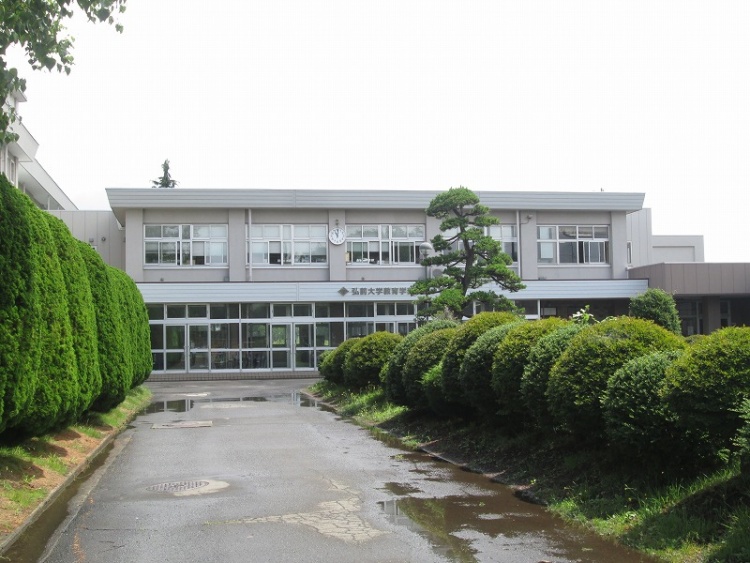 正面に植え込みが広がる、弘前大学教育学部附属小学校の二階建ての校舎外観です。