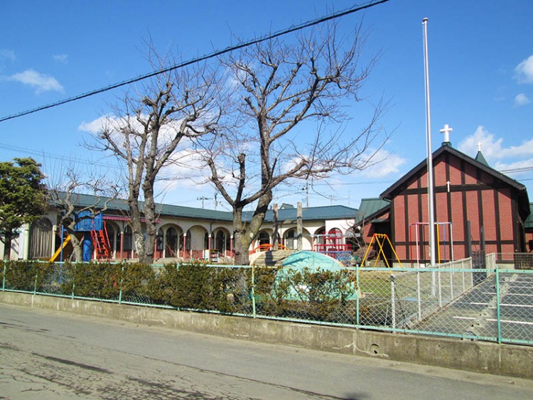 赤い外壁の建物と白い外壁の建物がある幼稚園の外観。遊具があり木々が立ち並んでいます。