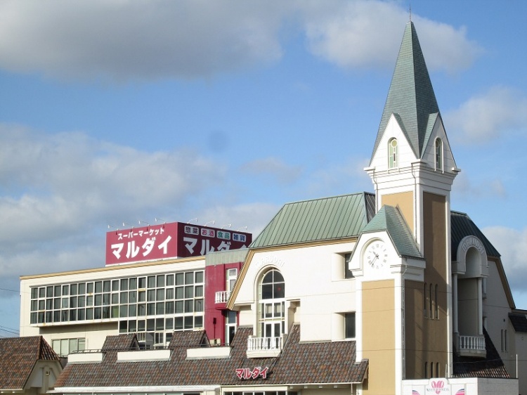 塔のある建物が特徴的な、赤い看板がついたスーパーマーケットマルダイ牛島店の外観です。