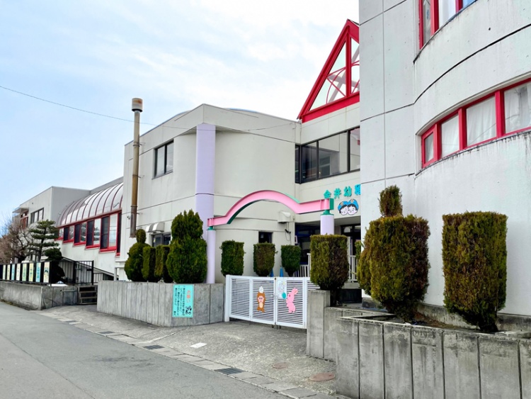 白の外壁に赤とピンクの屋根が特徴的な金井幼稚園の外観。植栽が植えられています。