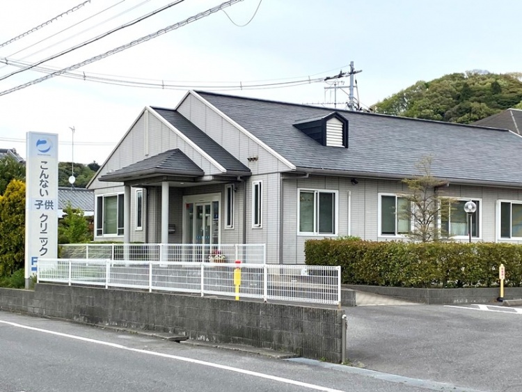 灰色の外壁と黒い屋根が特徴的なこんない子供クリニックの外観。フェンスと駐車場も見えます。