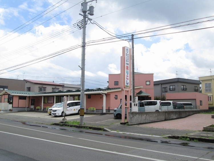 ピンク色の建物と駐車場があるこども園分園ほりこしの外観。手前には道路が見えます。