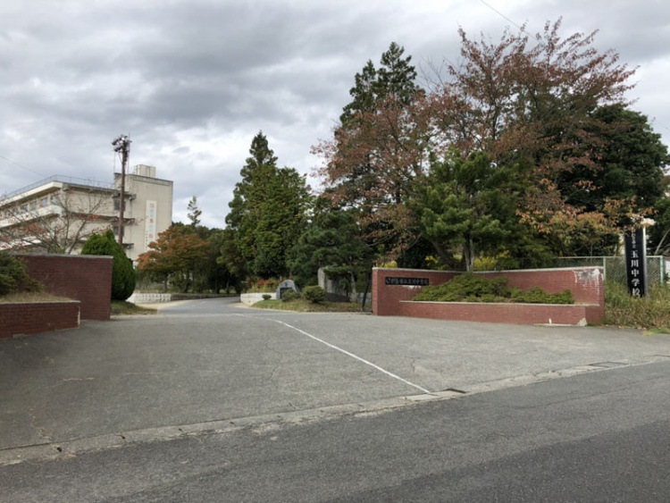 赤レンガの門が特徴的な玉川中学校の校舎の外観。奥には木々と校舎が見えます。