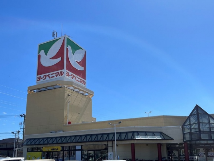 大きなヨークベニマルの看板がある建物の入り口。青空の下、ガラス屋根の部分も見える。