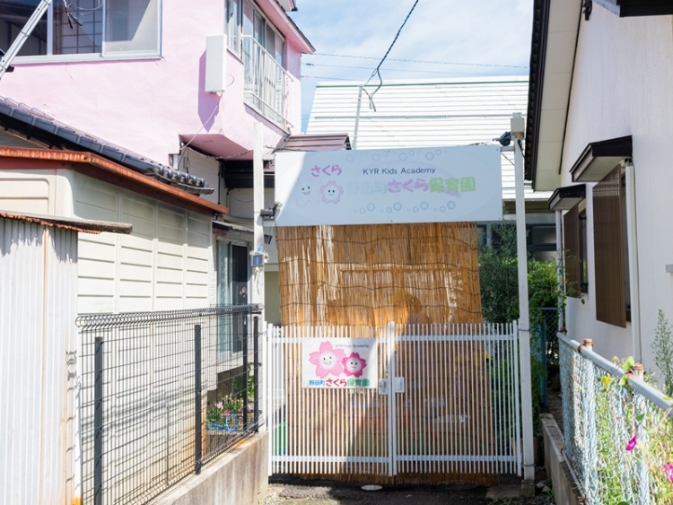 住宅街にあるさくら保育園の外観。白いゲートと薄茶色のよしずで飾られています。