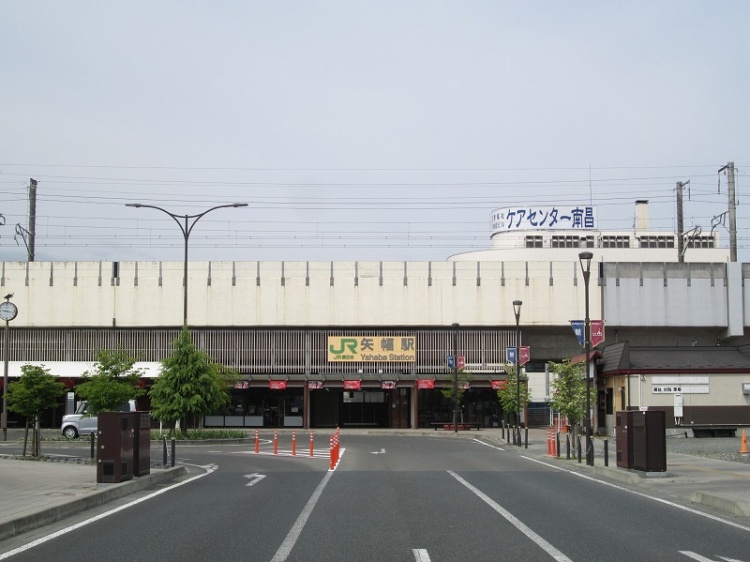 JR矢幅駅の正面入口。建物上部には駅名の看板があり、周囲には植栽や街灯があります。