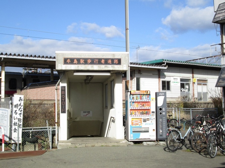 JR羽後牛島駅の外観。歩行者通路と自転車置き場、自動販売機が見えていて、背景に駅舎も見えます。