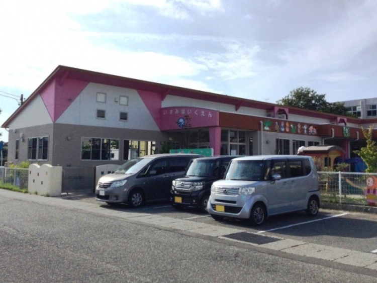 ピンクとグレーの外壁の泉保育園の外観。駐車場には数台の車が停められています。