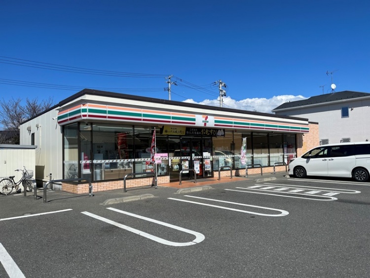 セブンイレブンの店舗外観。駐車場と自転車置き場もある。青空が広がる。