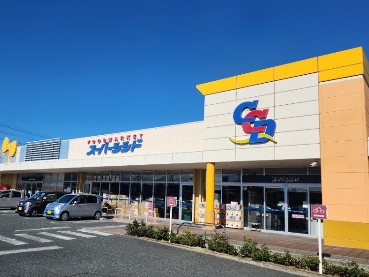 黄色と青が特徴的なスーパーシシド相馬リボン店の外観。駐車場には数台の車が停まっています。